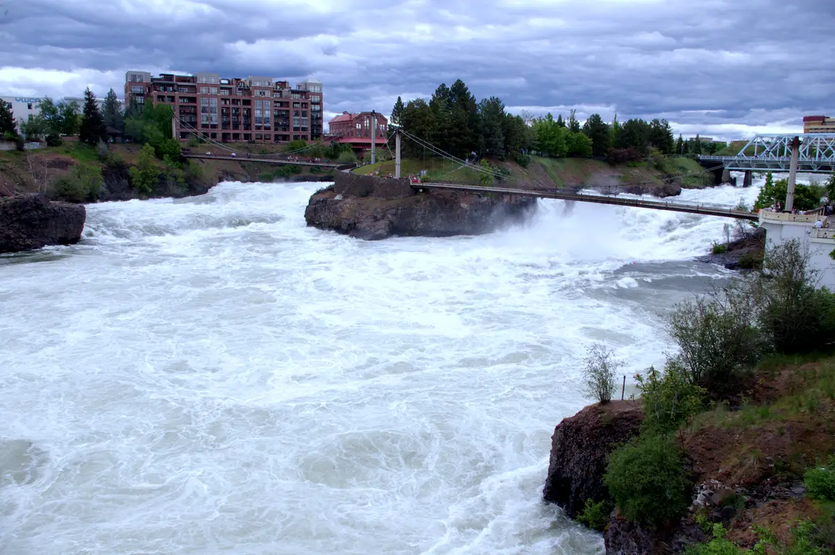 Upper Spokane Falls in daylight, with green trees and blue water.