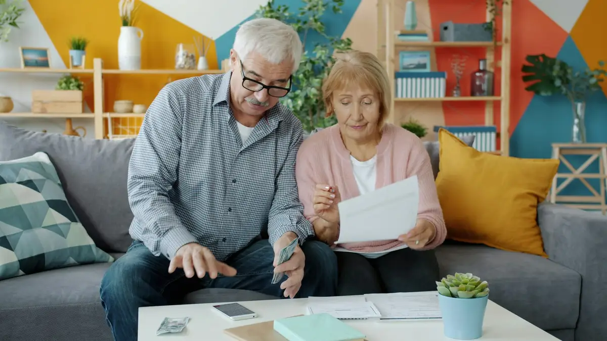 An older couple on a sofa at home, going through papers together.