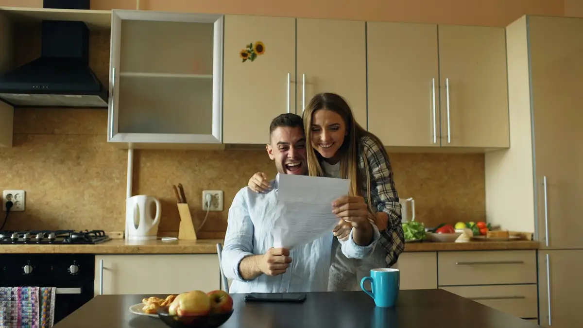 A couple standing at their kitchen counter, reading a letter together.