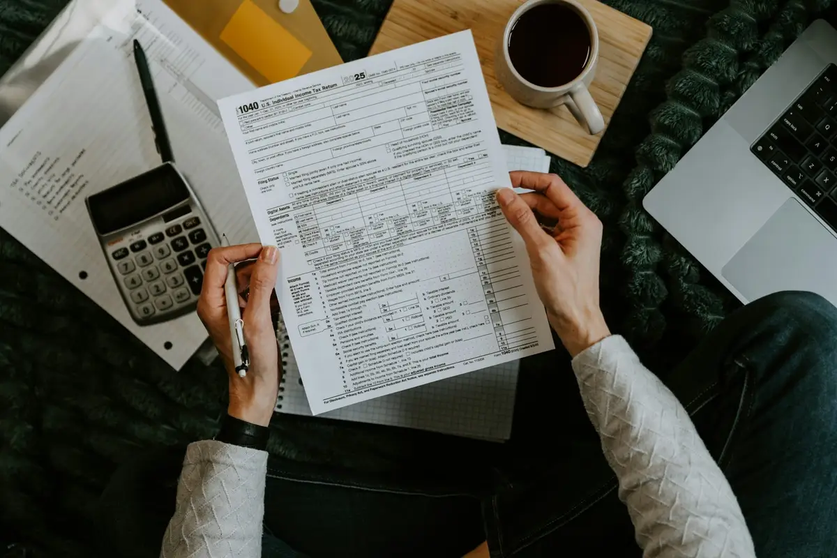 Hands holding a tax form over a desk with a calculator, a pen, and a cup of coffee.